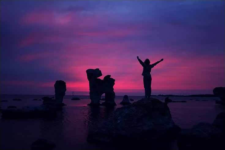 betvictro伟德体育日落照片的女人站在蓝色的海洋和粉红色和紫色的天空剪影。