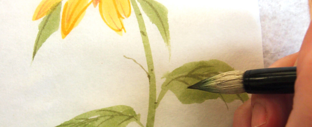 betvictro伟德体育一位艺术家用中国画笔在向日葵叶子上添加纹理的特写图像